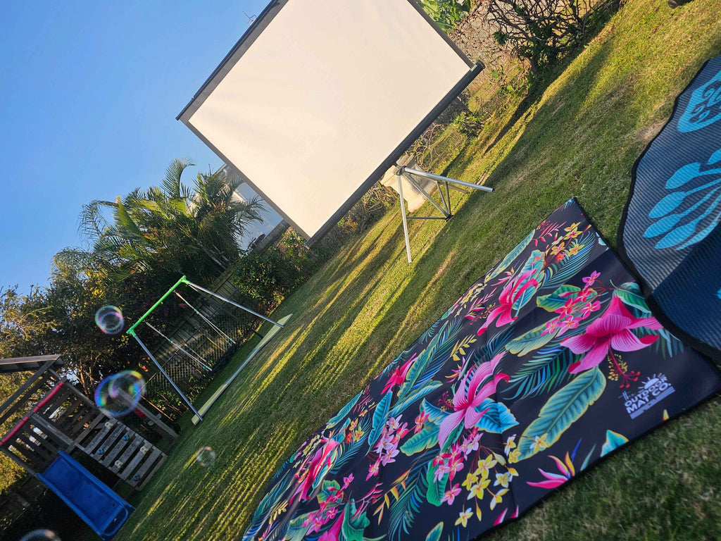 Tropical floral outdoor mat on grass near projector screen, perfect for backyard movie nights and picnics.