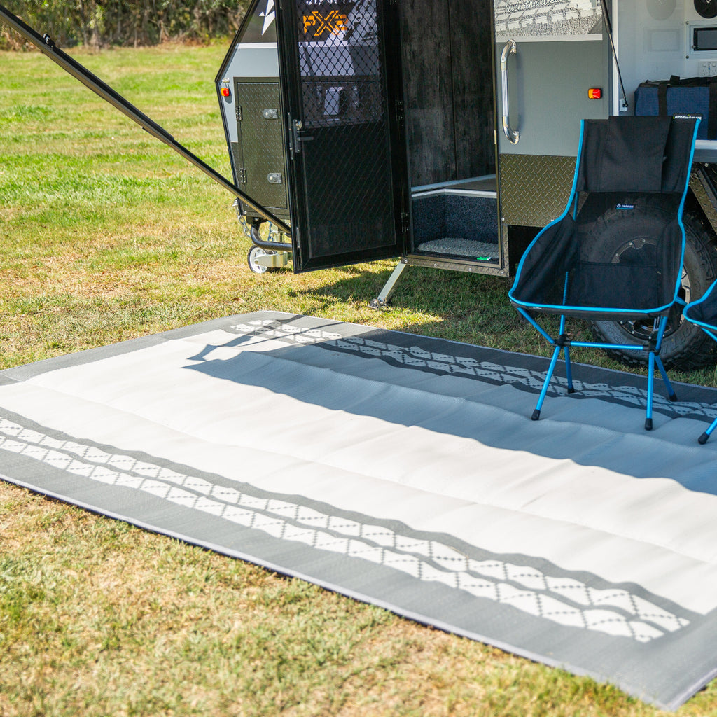 Recycled outdoor mat with geometric pattern on grass beside caravan and camping chair