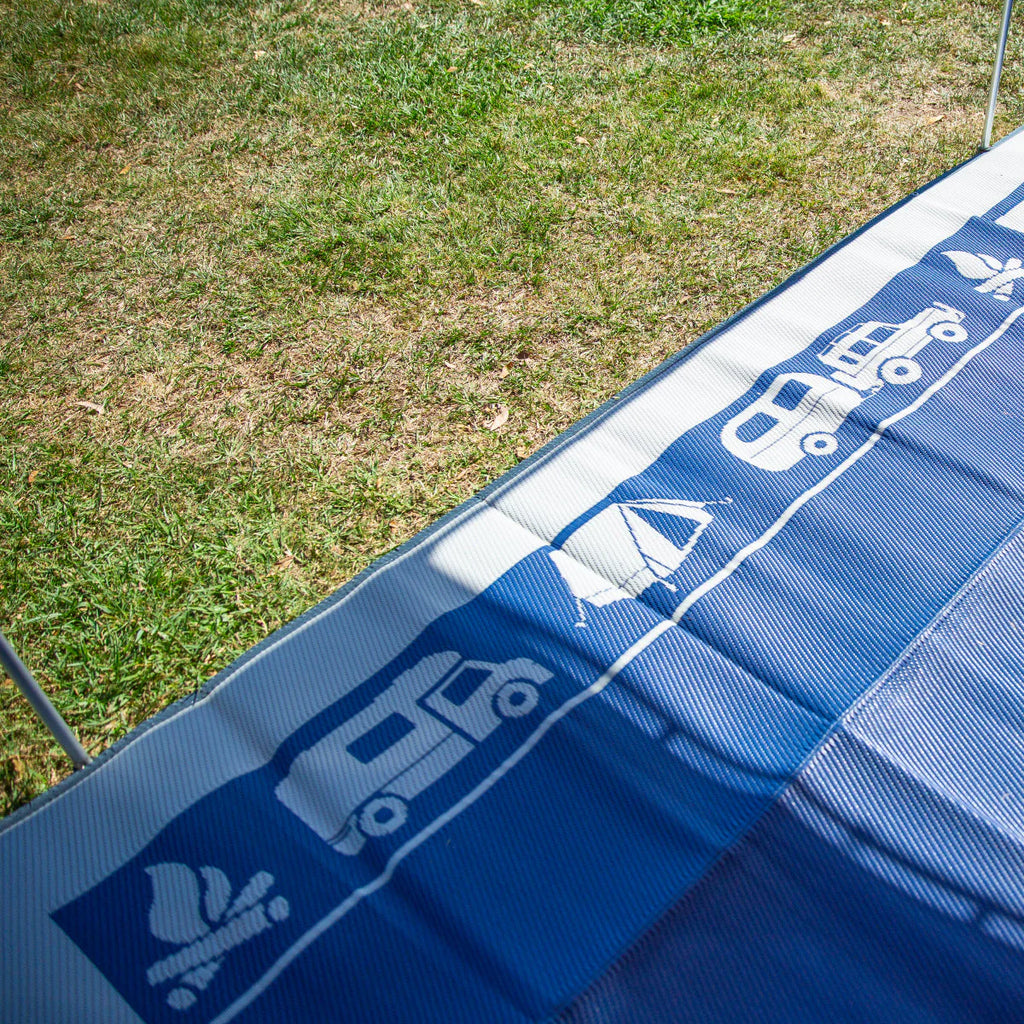 Blue recycled outdoor mat with caravan, tent, and camp icons on grass, perfect for camping and picnics.