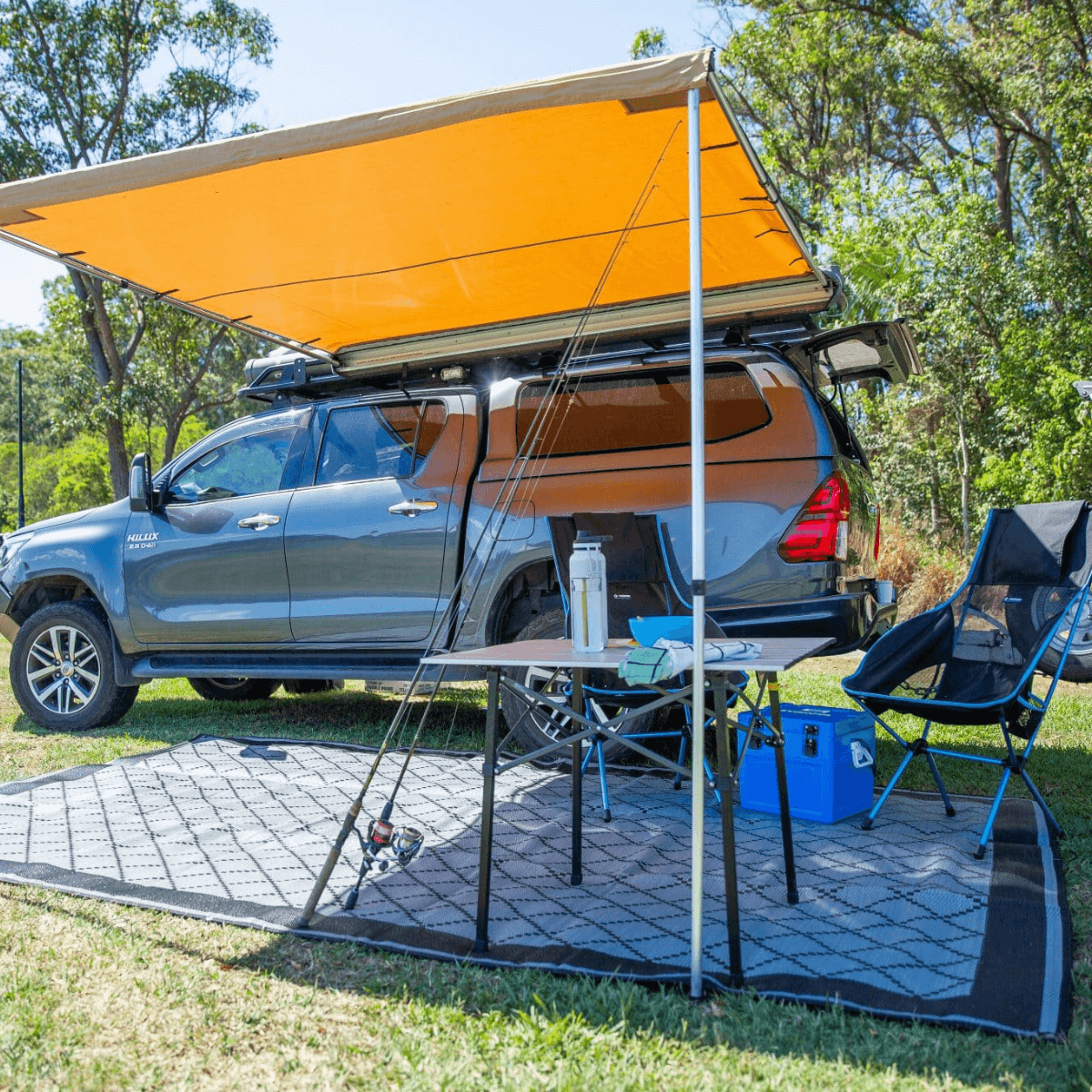 Recycled outdoor mat under camp setup with truck, table, chairs, and awning in grassy area