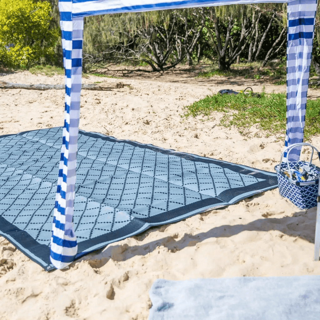Blue patterned recycled outdoor mat on sandy beach under striped canopy, perfect for picnics and beach days