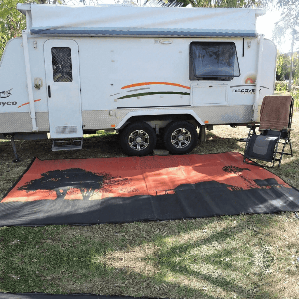 Recycled outdoor mat with sunset design under caravan, perfect for camping and picnics on grass