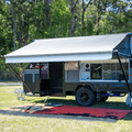 Red and black recycled outdoor mat under caravan awning on grass, perfect for camping and picnics