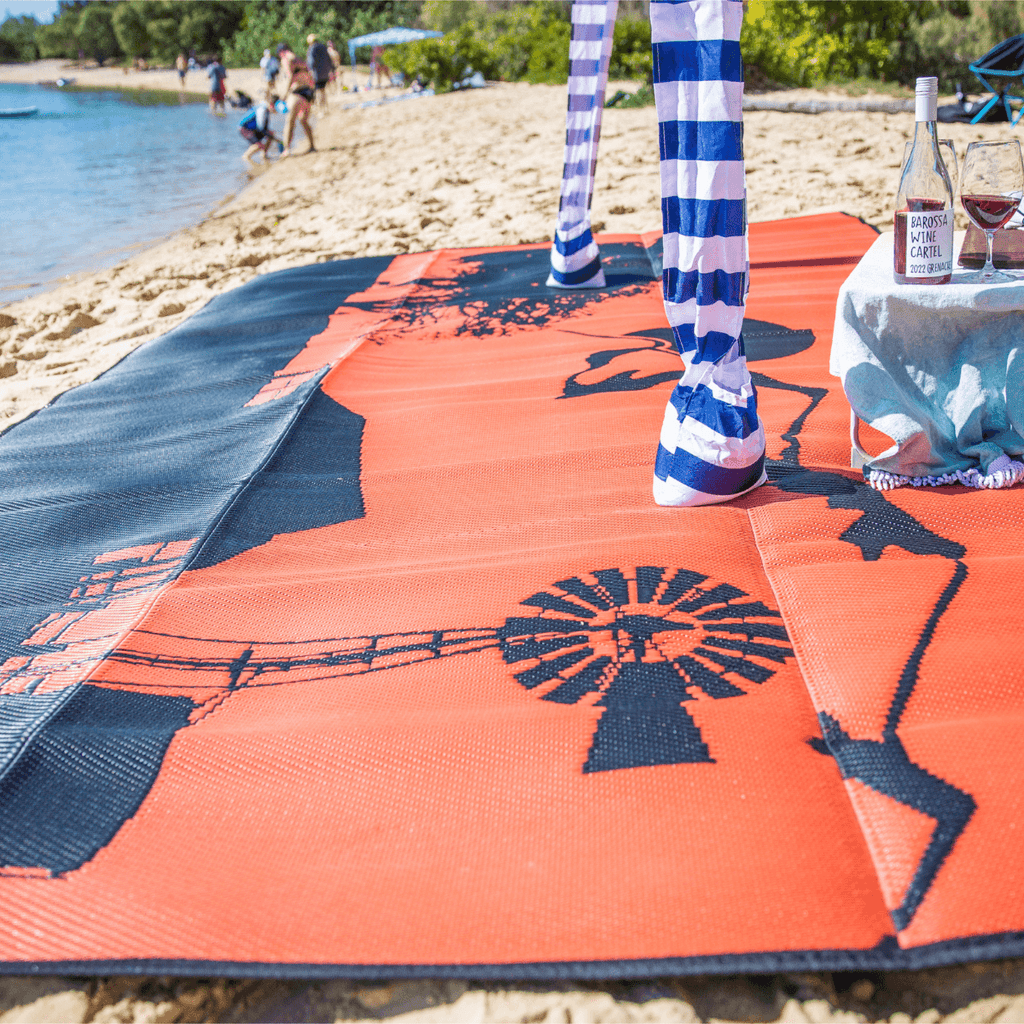 Orange and navy recycled outdoor mat with windmill design on sandy beach, perfect for picnics and beach days