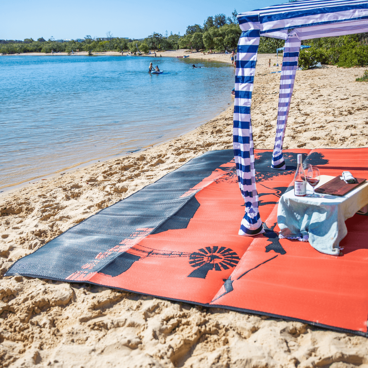 Eco-friendly outdoor mat on sandy beach with picnic setup under striped canopy, perfect for beach days and picnics.