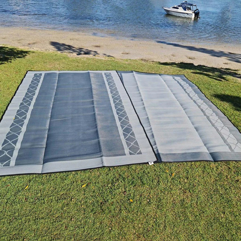 Recycled outdoor mat on grass near beach, ideal for picnics, camping, or caravan trips with stylish geometric pattern.