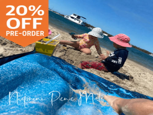Blue neoprene picnic mat on beach with kids playing, perfect for outdoor adventures and pre-order discount