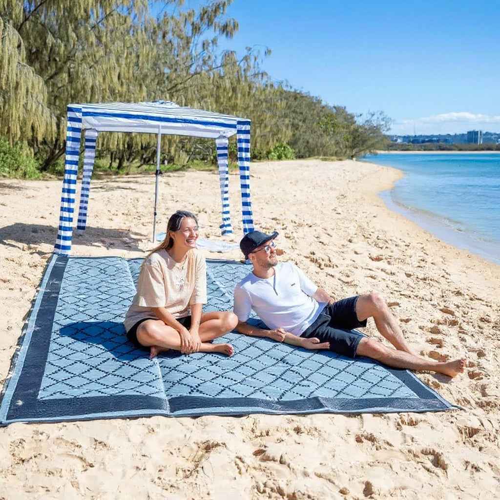 Couple relaxing on eco-friendly beach mat under striped canopy, perfect for sand, picnics, and outdoor adventures.