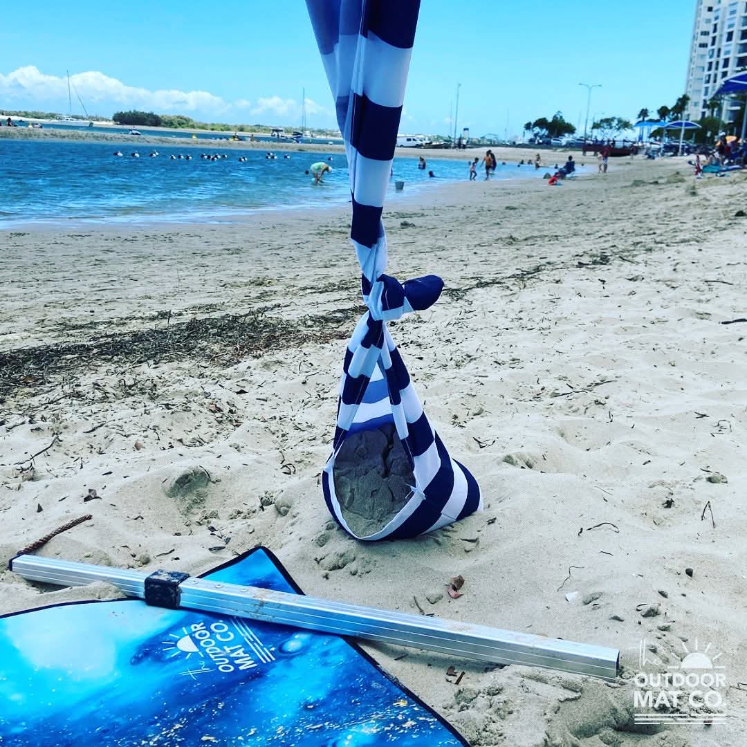 Blue beach mat with sand anchor bag on sandy shore, perfect for beach days and picnics
