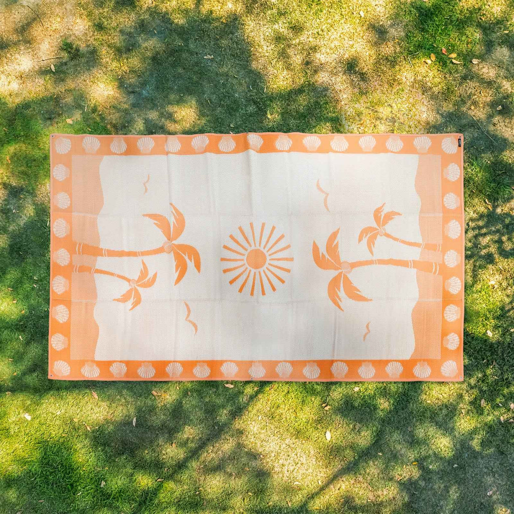 Orange palm tree and sun patterned outdoor mat on grass, perfect for beach, picnic, or camping
