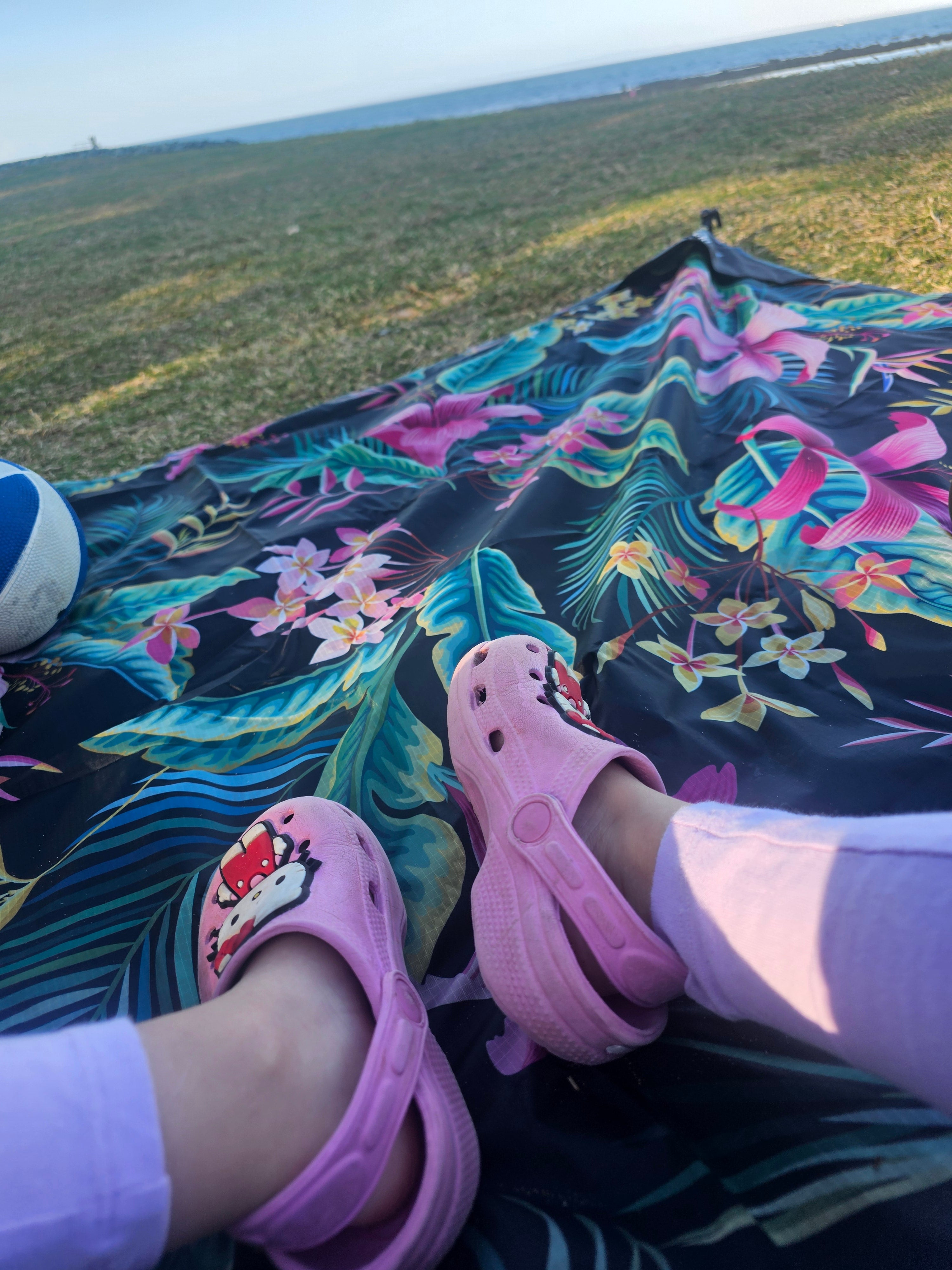Tropical print outdoor mat on grass near beach, child's pink Crocs, perfect for picnics & camping