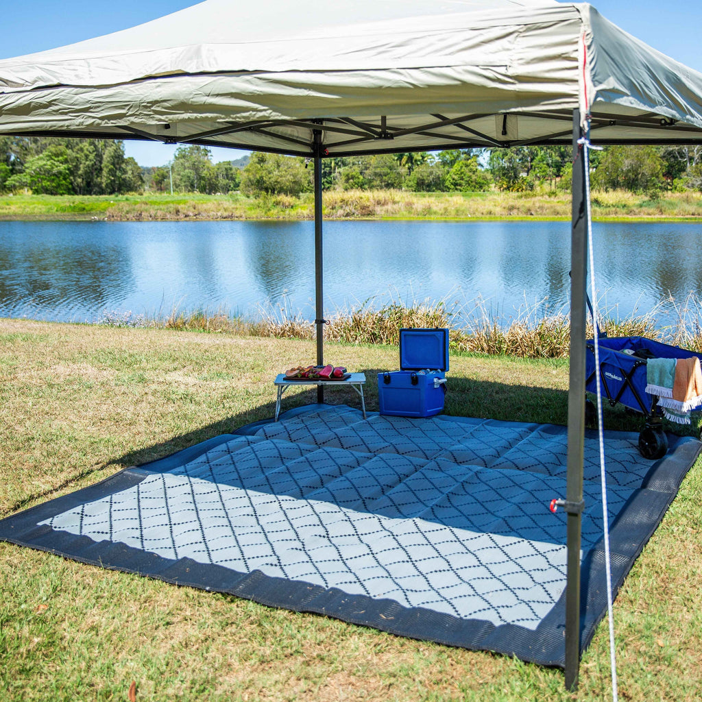 Blue and white patterned outdoor mat under a canopy by a lake, perfect for picnics and camping.
