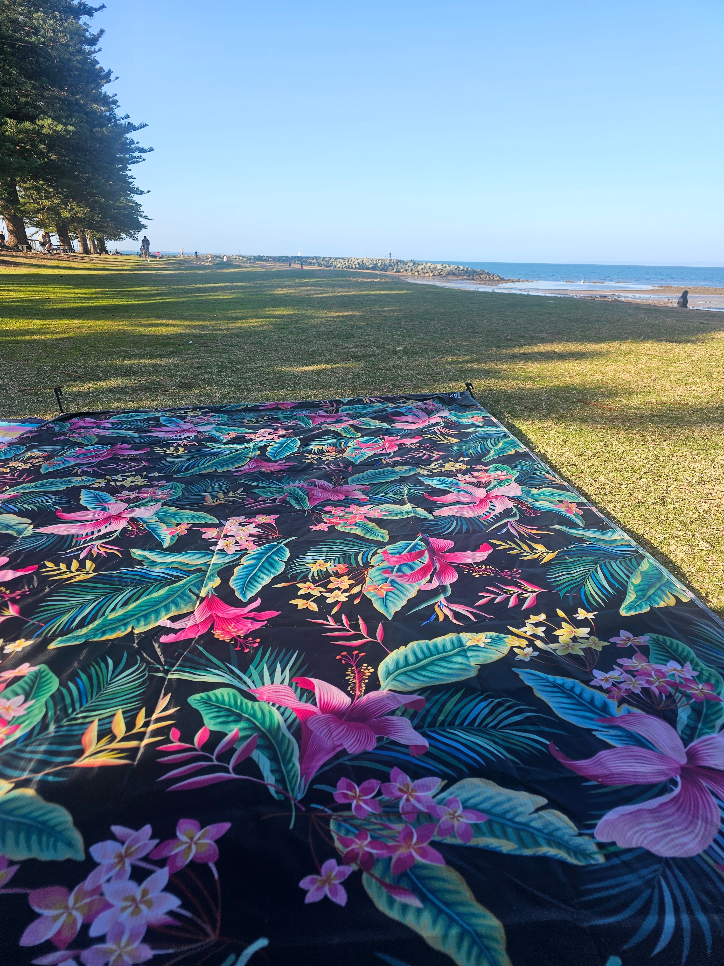 Tropical floral outdoor mat on grass near beach, perfect for picnics, camping, or caravan trips