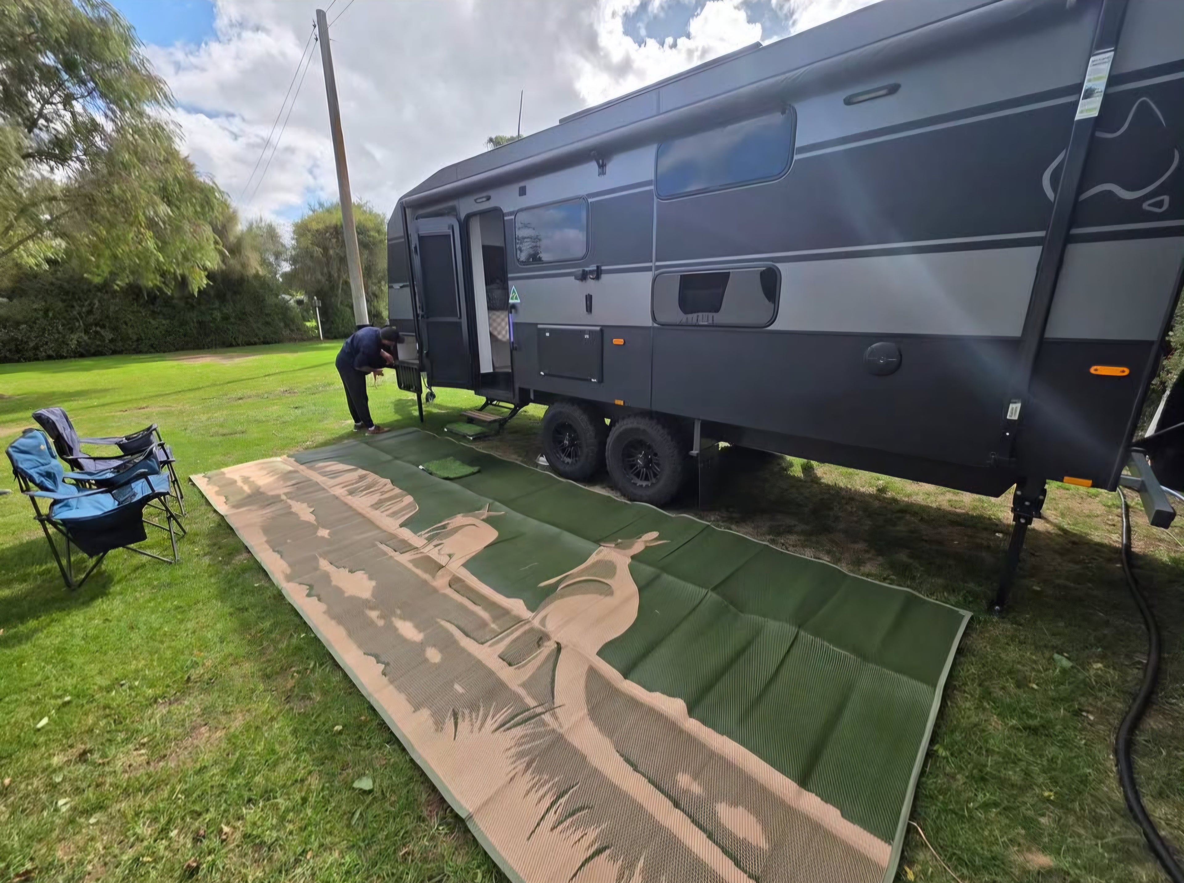 Green recycled outdoor mat with desert print beside caravan, perfect for camping, picnics, and beach days.