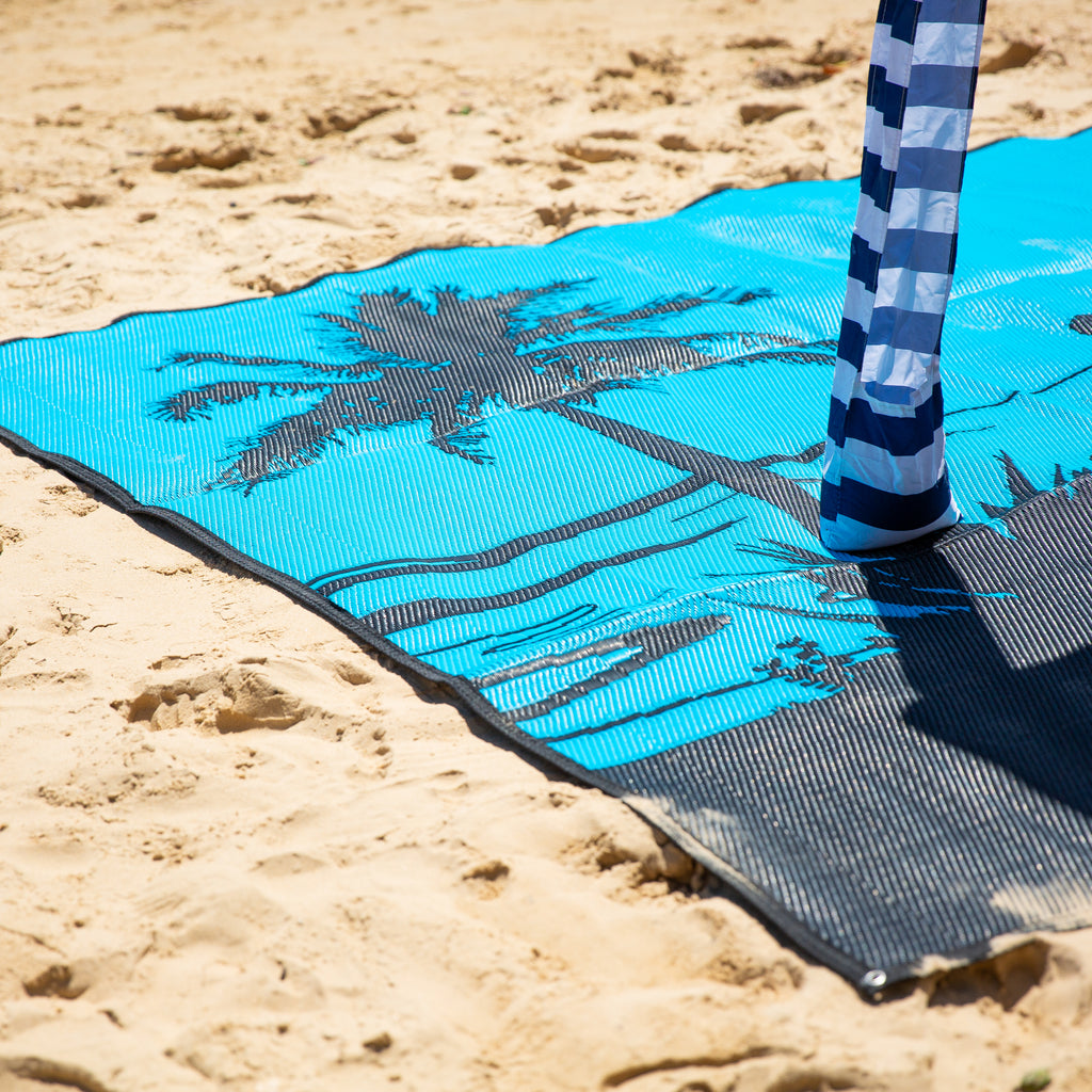 Blue beach mat with palm tree design on sand, perfect for beach days and picnics