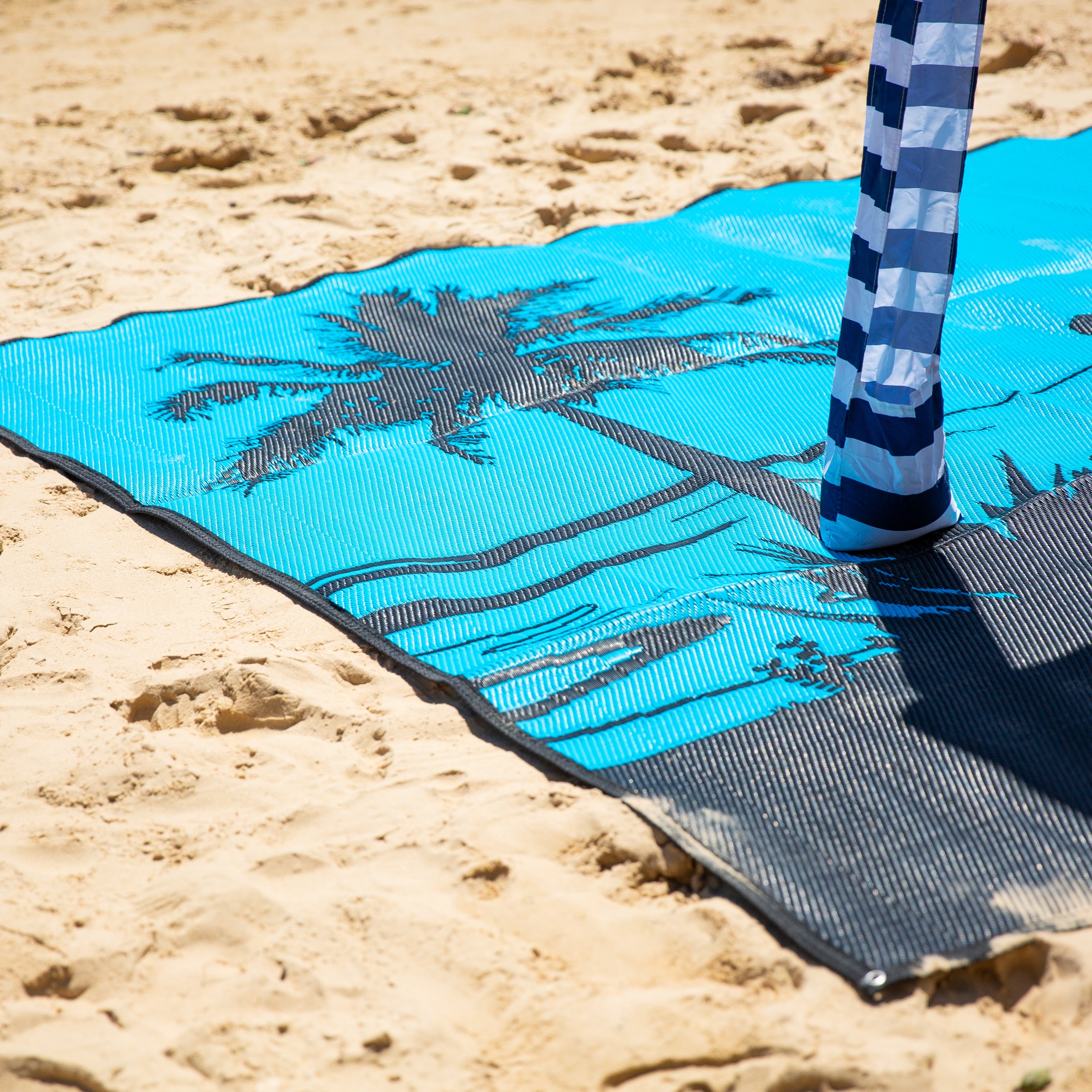 Blue beach mat with palm tree design on sand, perfect for beach days and picnics