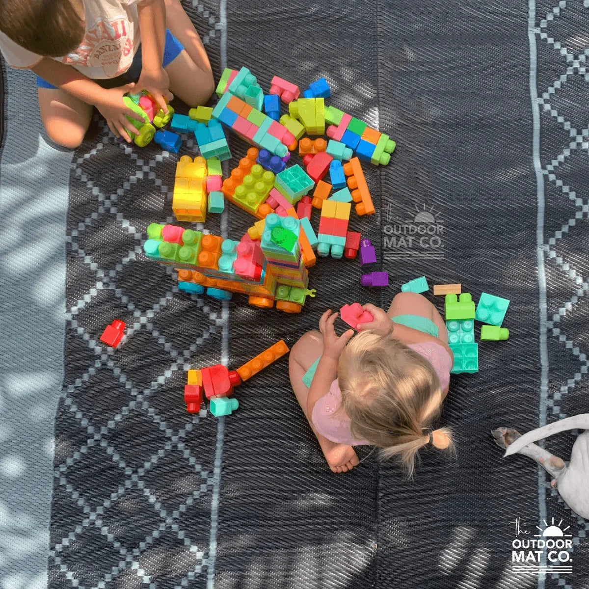Kids playing with colorful blocks on a recycled outdoor mat for picnics, camping, or beach days