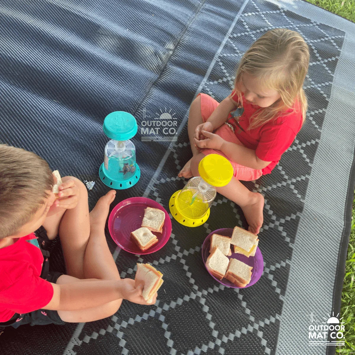 Kids enjoying sandwiches on a recycled outdoor picnic mat, perfect for beach, camping, or park outings.