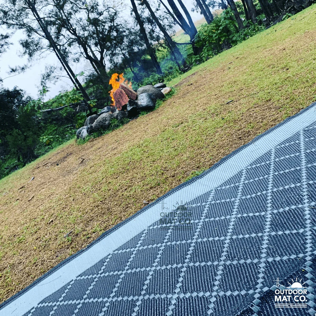 Recycled outdoor mat with geometric pattern on grass near campfire, perfect for camping and picnics