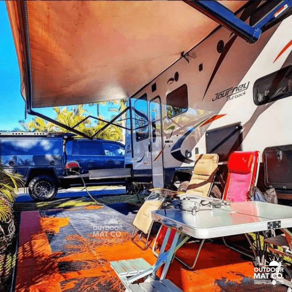 Vibrant orange recycled outdoor mat under caravan awning with camping chairs and table, perfect for beach or picnic trips.
